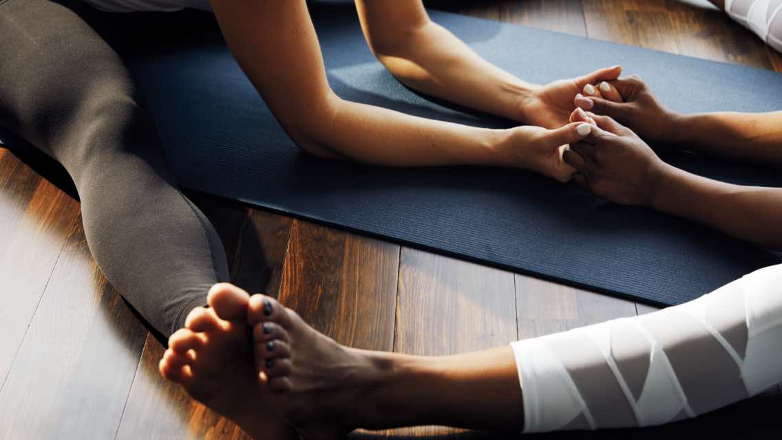 Two woman stretching and holding hands in a yoga class at Life Time. 