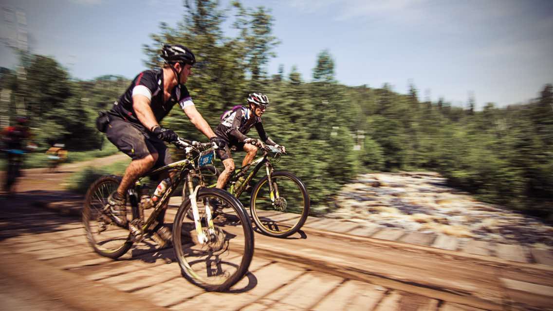 Two men riding a bicycle outdoor at a Life Time Athletic Event 