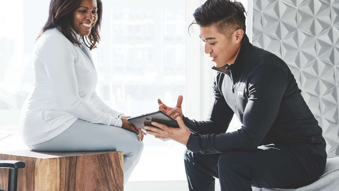 A Life Time dietician explains to a Life Time member their lab result tests in a light, bright and airy room with white ceramic tiles on the walls. 