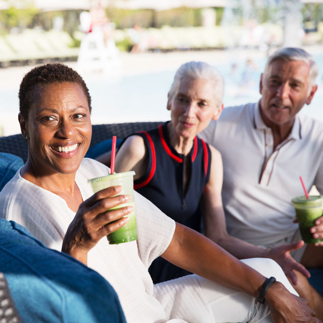 A female trainer in a black, zip-up jacket talks to an older man with silver hair who is wearing a white, short-sleeve t-shirt