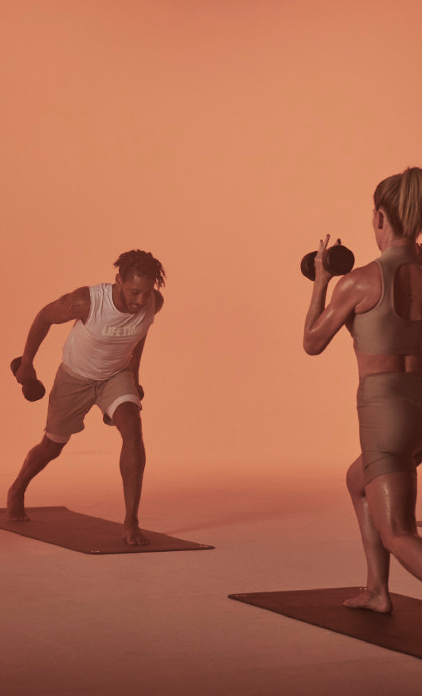a group fitness class lifts dumbells while lunging
