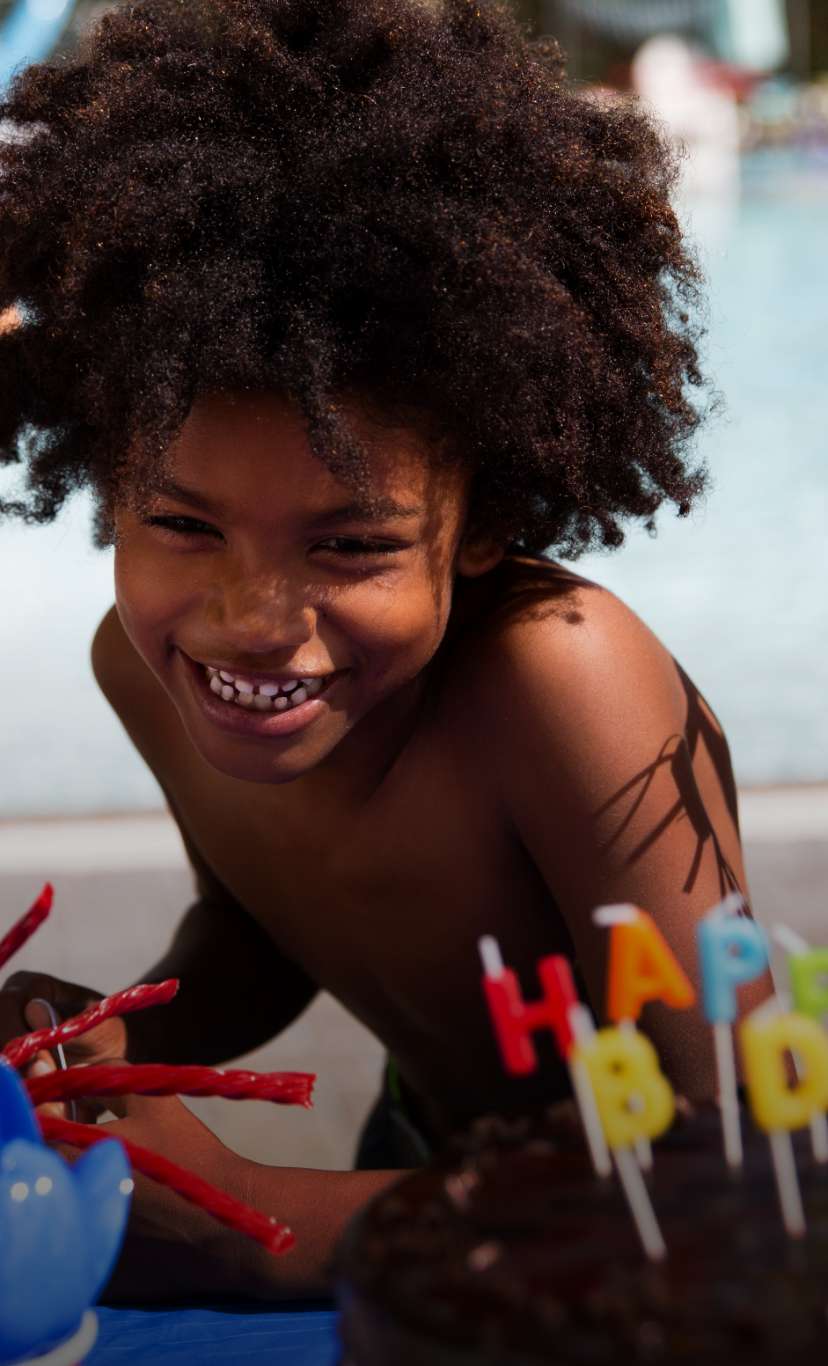 a group of children gather around a boy before he blows out candles on a birthday cake