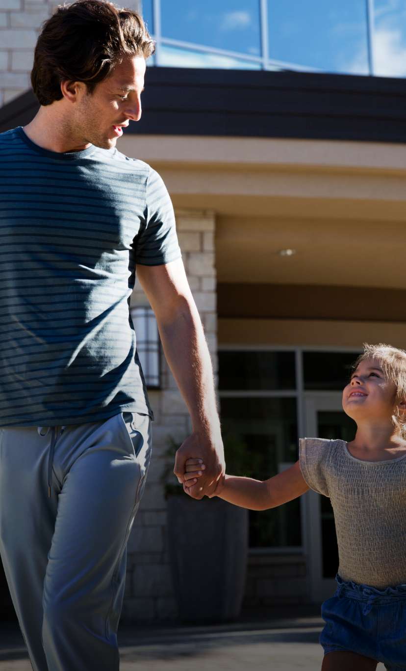 a young girl smiles up at her dad while holding his hand