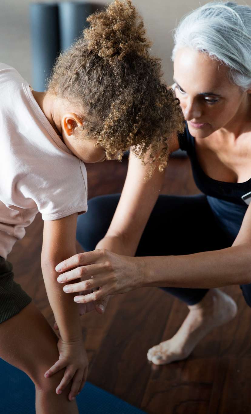 An instructor helps a child with a yoga pose
