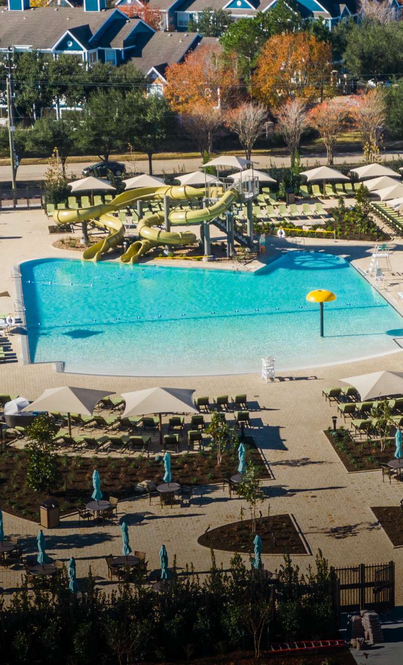 A view of an outdoor pool deck with a zero depth entry pool and waterslides