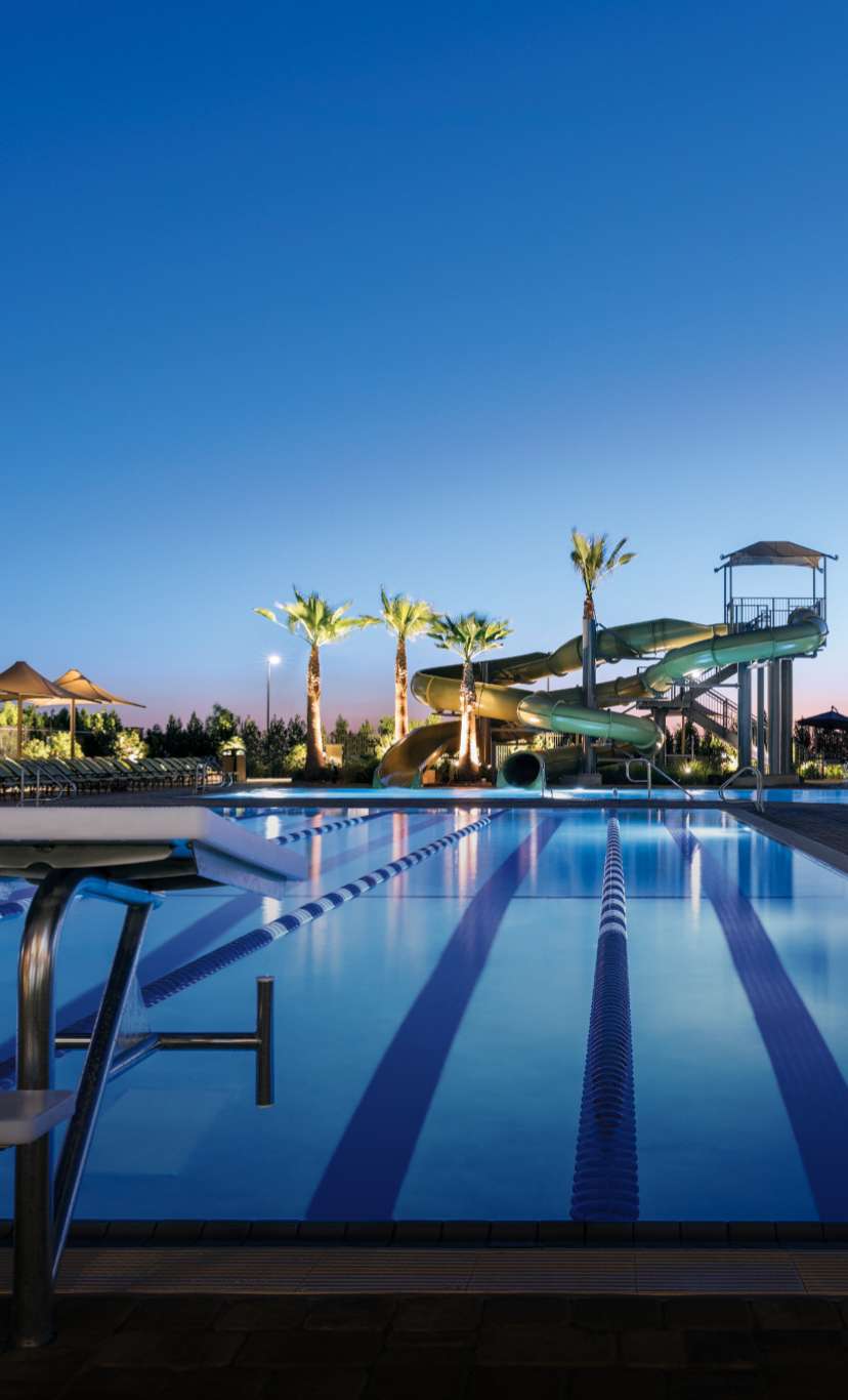 An outdoor lap pool with waterslides in the distance at dusk