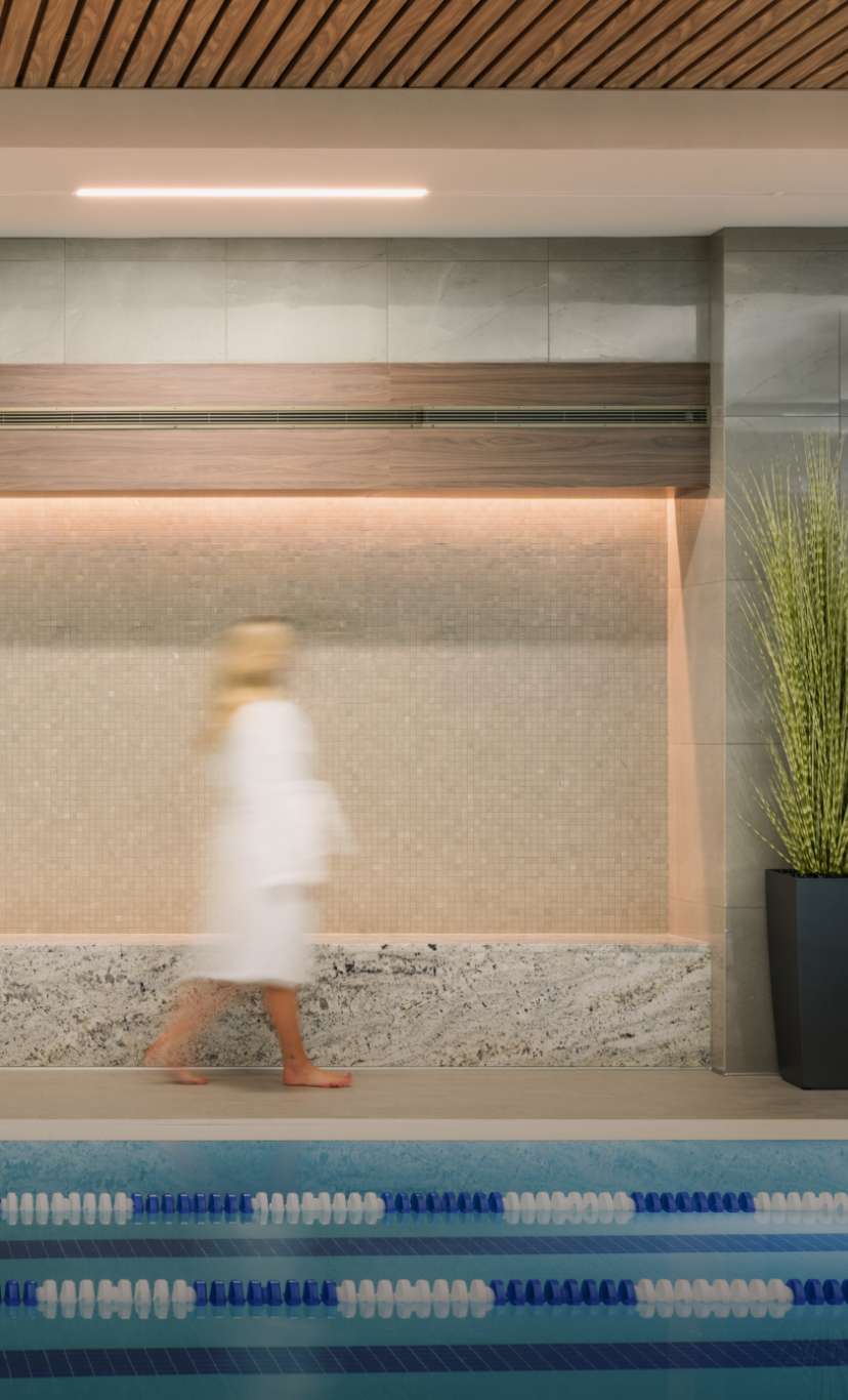 a woman walks on the deck of an indoor lap pool