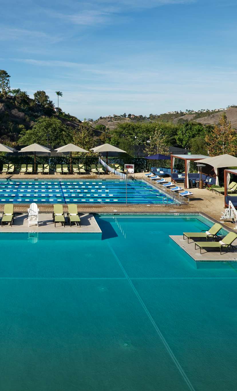 an expansive outdoor pool area with leisure and lap pool, deck chairs and umbrellas