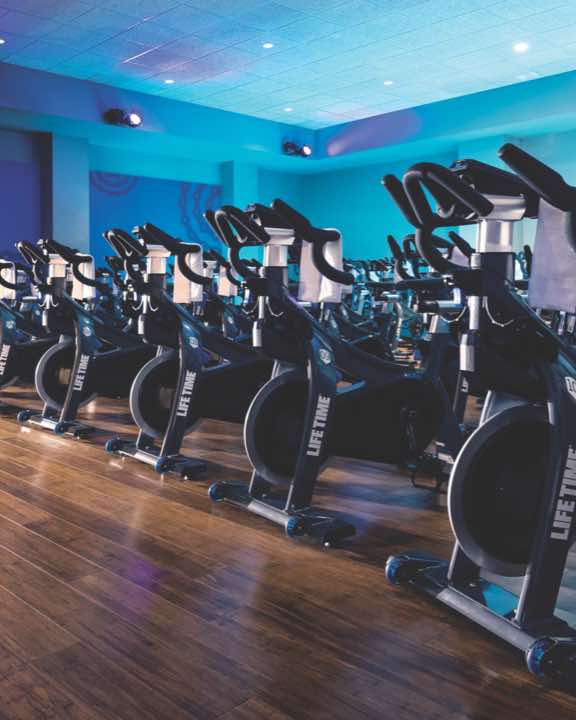 Colorfully lit indoor cycle studio with rows of indoor bikes 