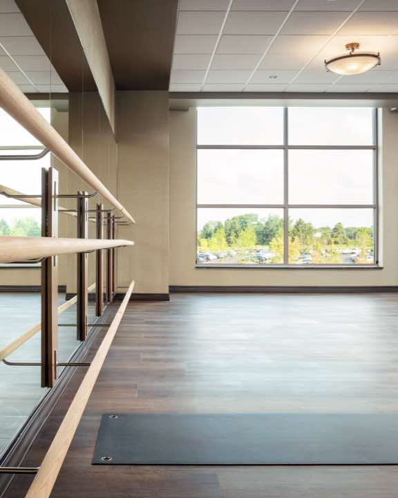 Sunlit group fitness studio with wooden floor, mirrored wall and barre