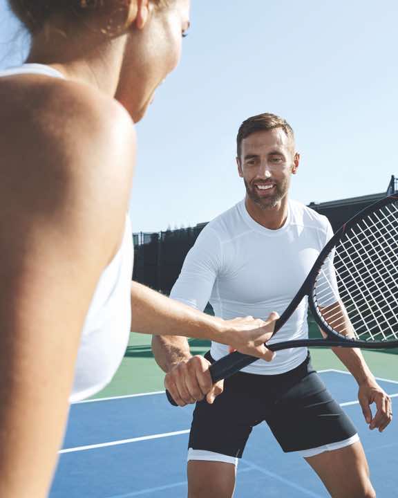 Man and woman playing tennis on an outdoor tennis court at Life Time