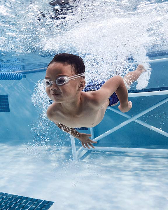 Little boy taking swimming lessons in a pool at Life Time 