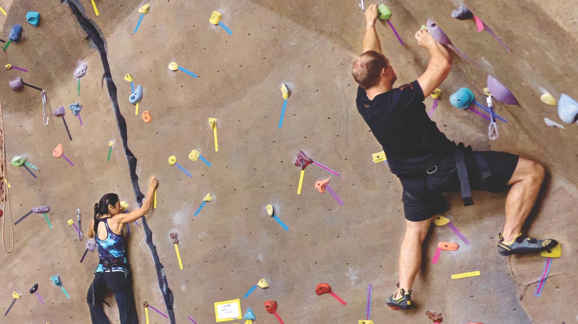a man and a women scaling an indoor rockclimbing wall at a life time location