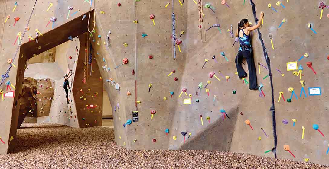A coach watching two adults on an indoor climbing wall