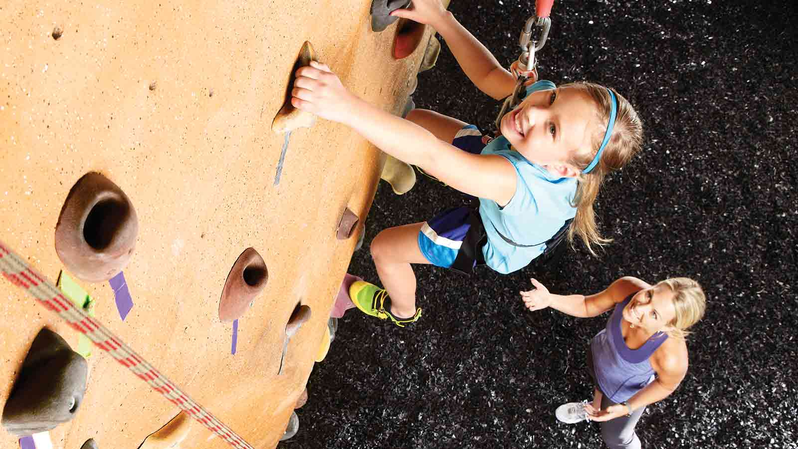 A girl climbing a rockwall with a woman spotting her below