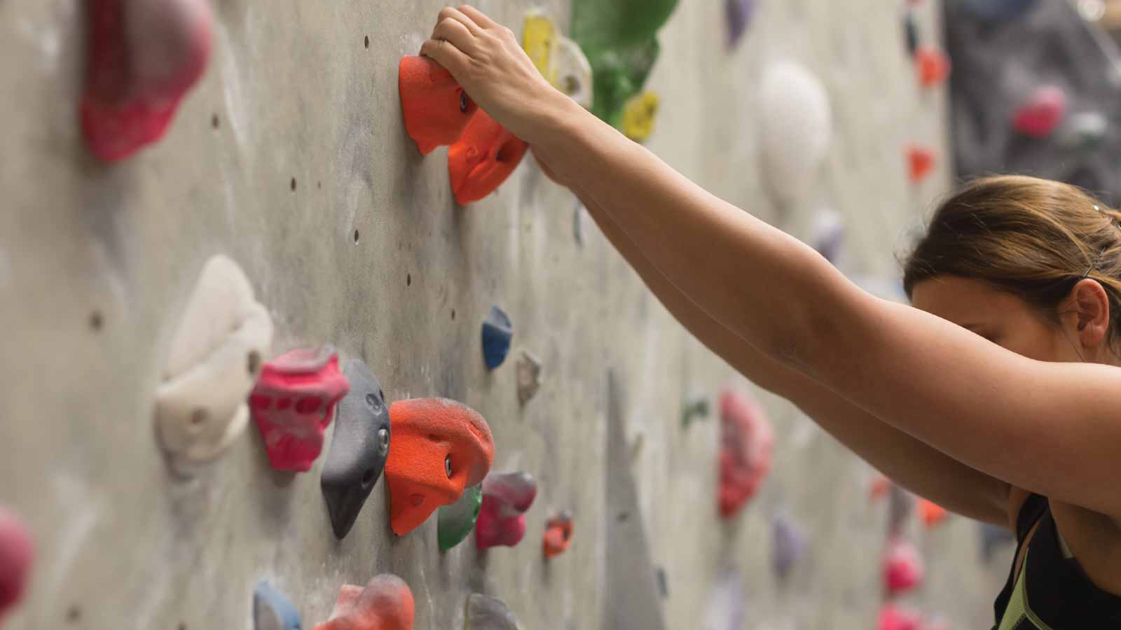 A woman reaching to grab a hold above her while bouldering