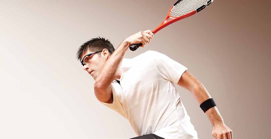 A man wearing squash athletic gear taking a swing on the court