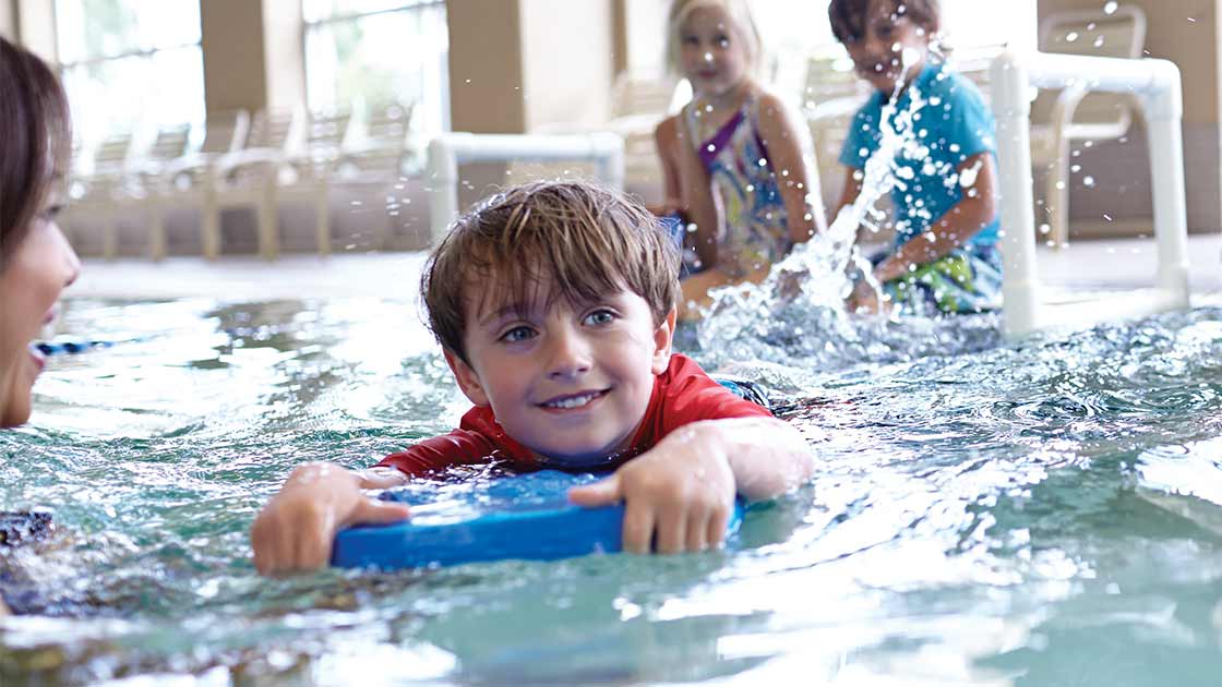 A boy using a kickboard in a youth swim class