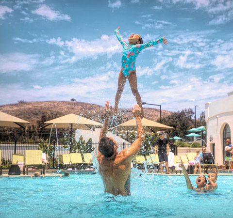 man playing with a hild in an outdoor pool
