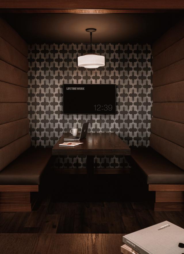 2 semi private office areas against a brick wall. The 2 desks feature wood grained tops, office chairs, computer monitors, and desk lamps, with a wall shelf.